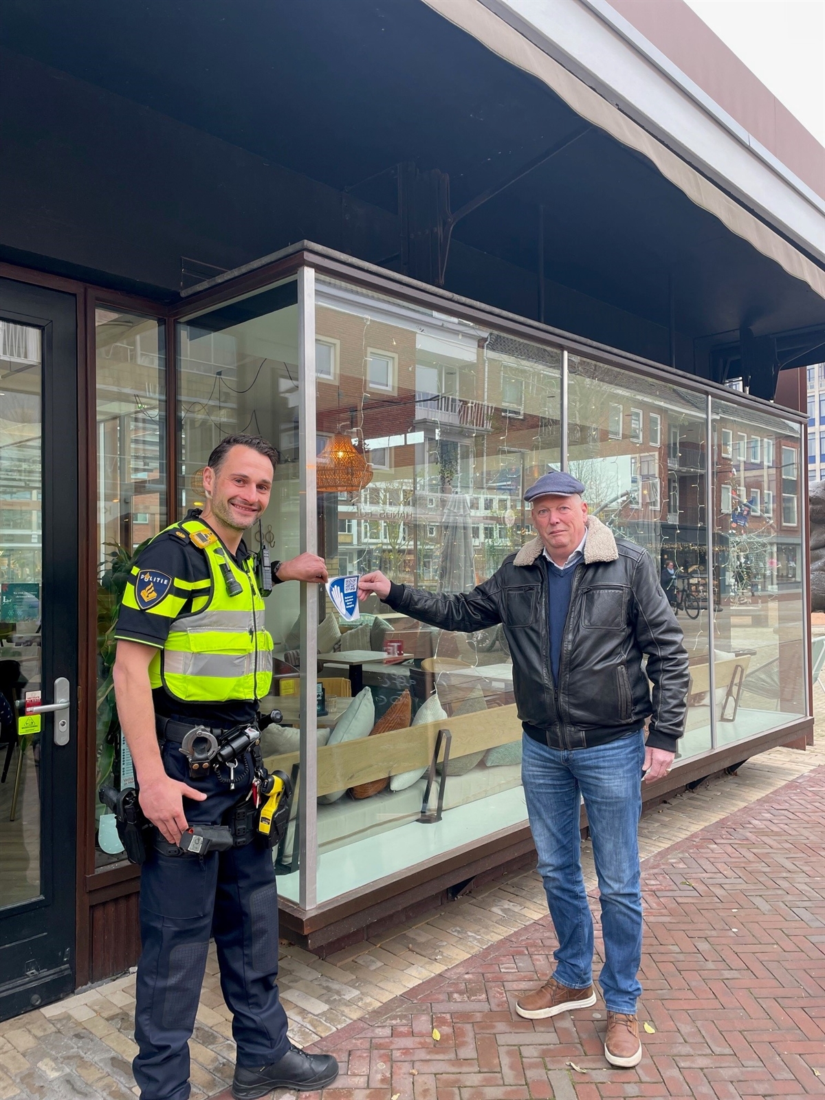 Bas van den Heuvel (wijkagent horeca binnenstad) en Berto Mulders (voorzitter Koninklijke Horeca Nederland, afdeling Hengelo) plakken de deursticker bij één van de deelnemende horecazaken. 